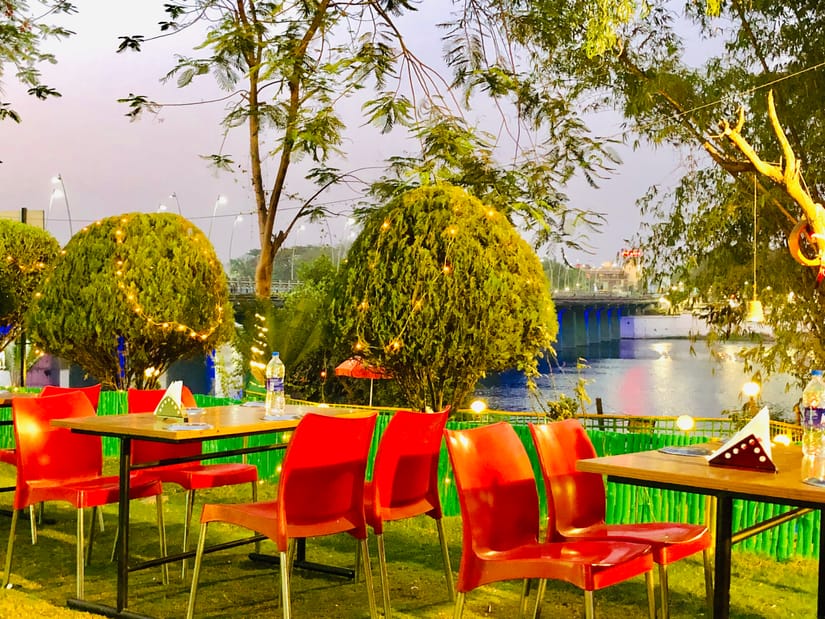 Open-air riverside dining with tables and red chairs at VITS Kamats Resort Silvassa