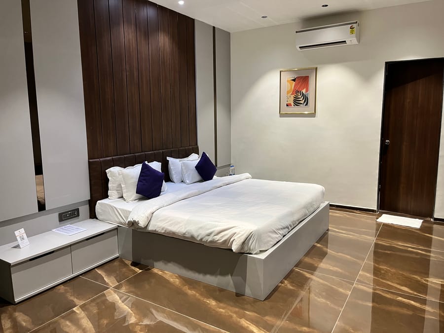 A king bed next to a side table in the super deluxe room at VITS Jamnagar, Mithoi