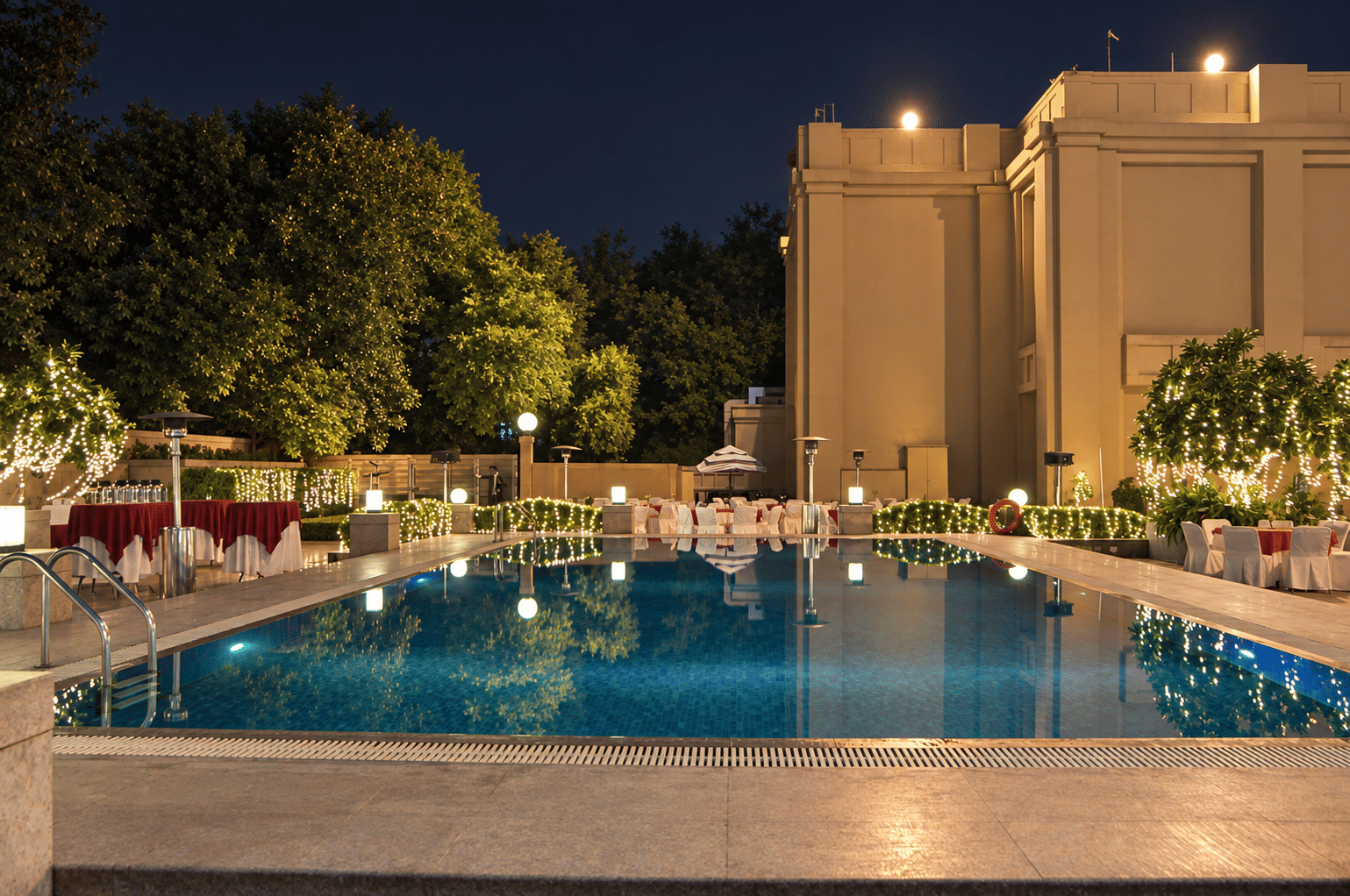 The outdoor pool at night, lit from within, with string lights in the trees beyond