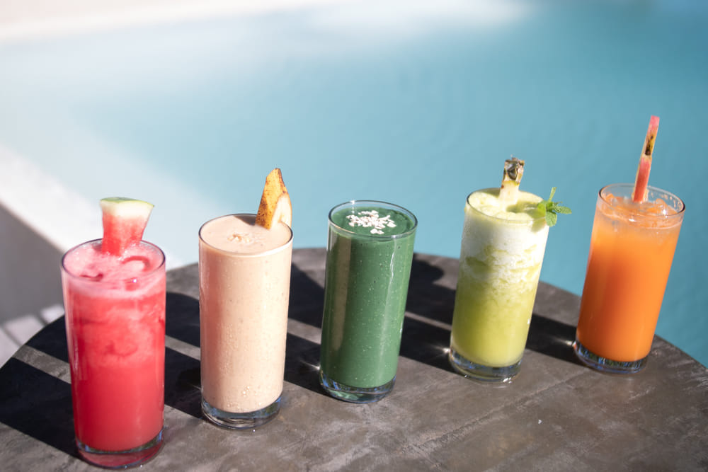 5 colorful fruit drinks including watermelon, banana, green smoothie, pineapple mint, and orange juice lined up on a table by the pool at Bravo Beach Resort Siargao