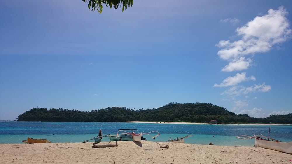 Outrigger boats on a white sand beach facing Anahawan and La Januza Islands across turquoise water, Siargao