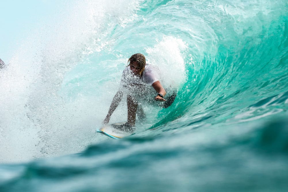 A surfer crouched low on his board, riding inside a barreling turquoise wave with white spray curling overhead at Cloud 9, Siargao