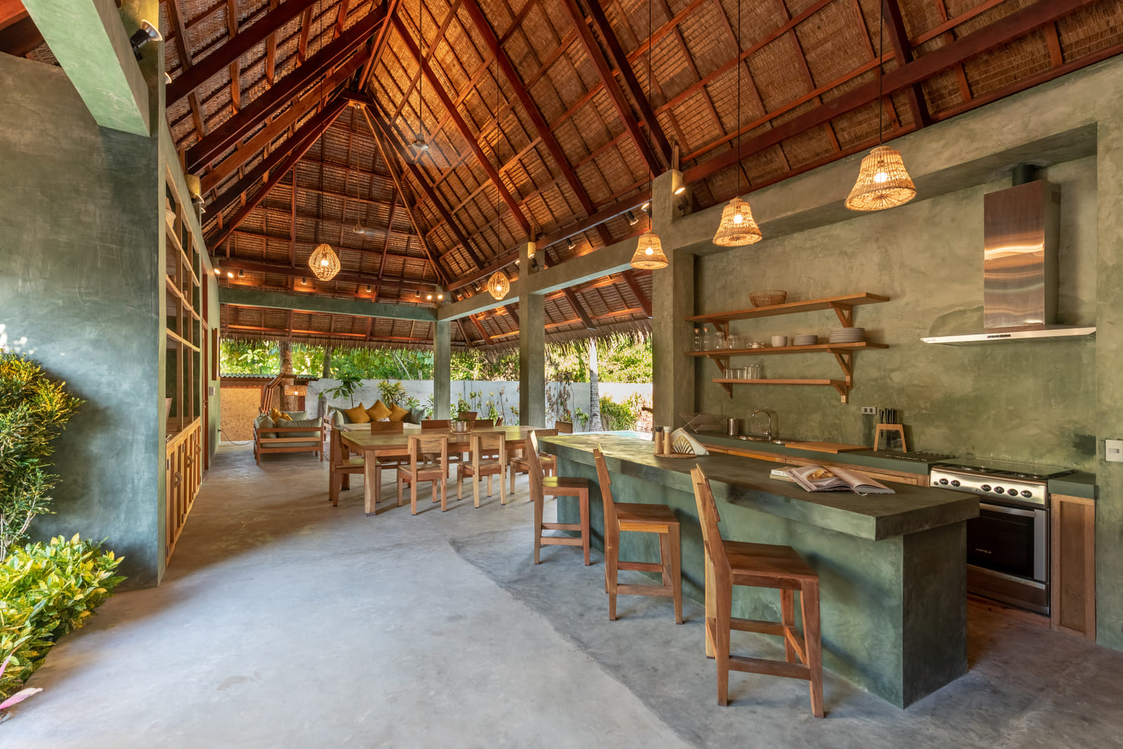 Open-air kitchen and dining pavilion at Tadhana Villa, Bravo Beach Resort Siargao, with a thatched roof, wooden table, and stone bar counter
