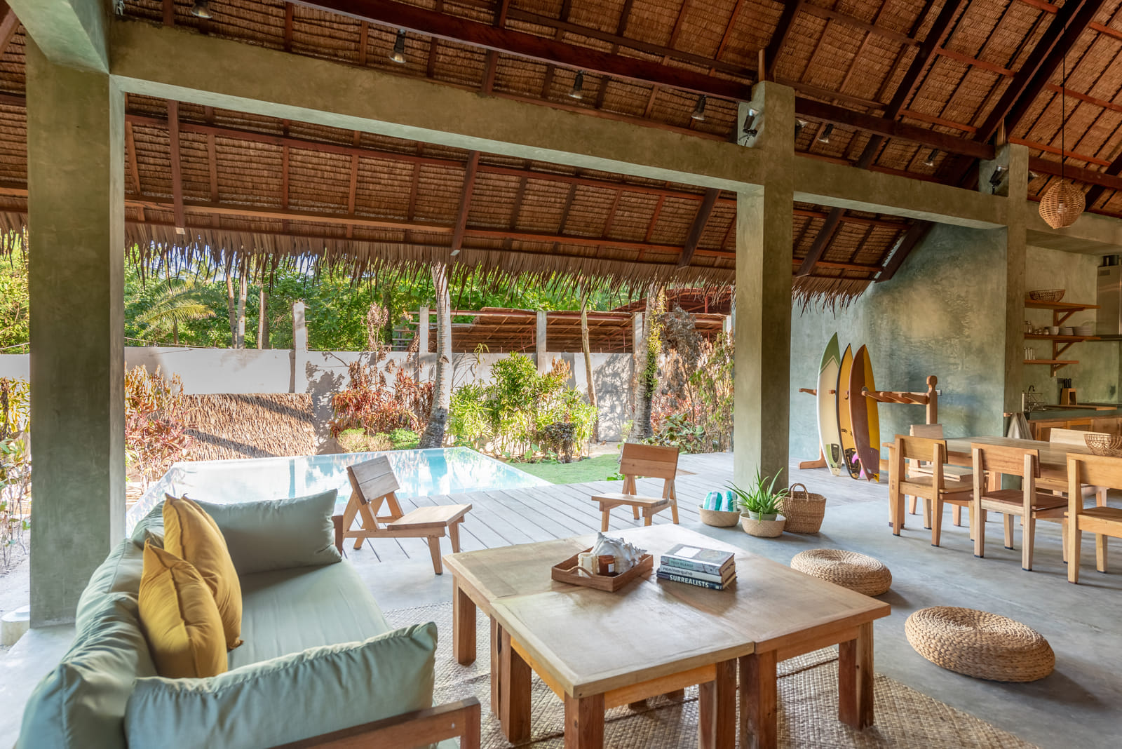 Lounge and pool area at Tadhana Villa, Bravo Beach Resort Siargao, with a sage sofa, mustard cushions, surfboards, and a thatched-roof pavilion