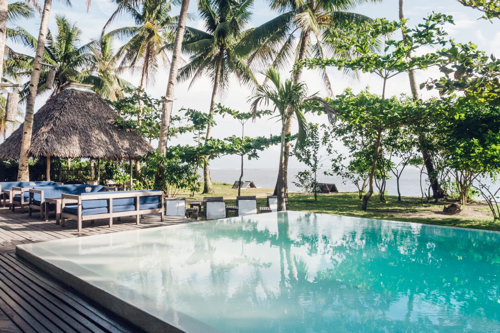 Infinity pool at Bravo Beach Resort Siargao lined with wooden daybeds, framed by coconut palms and a thatched pavilion overlooking the sea