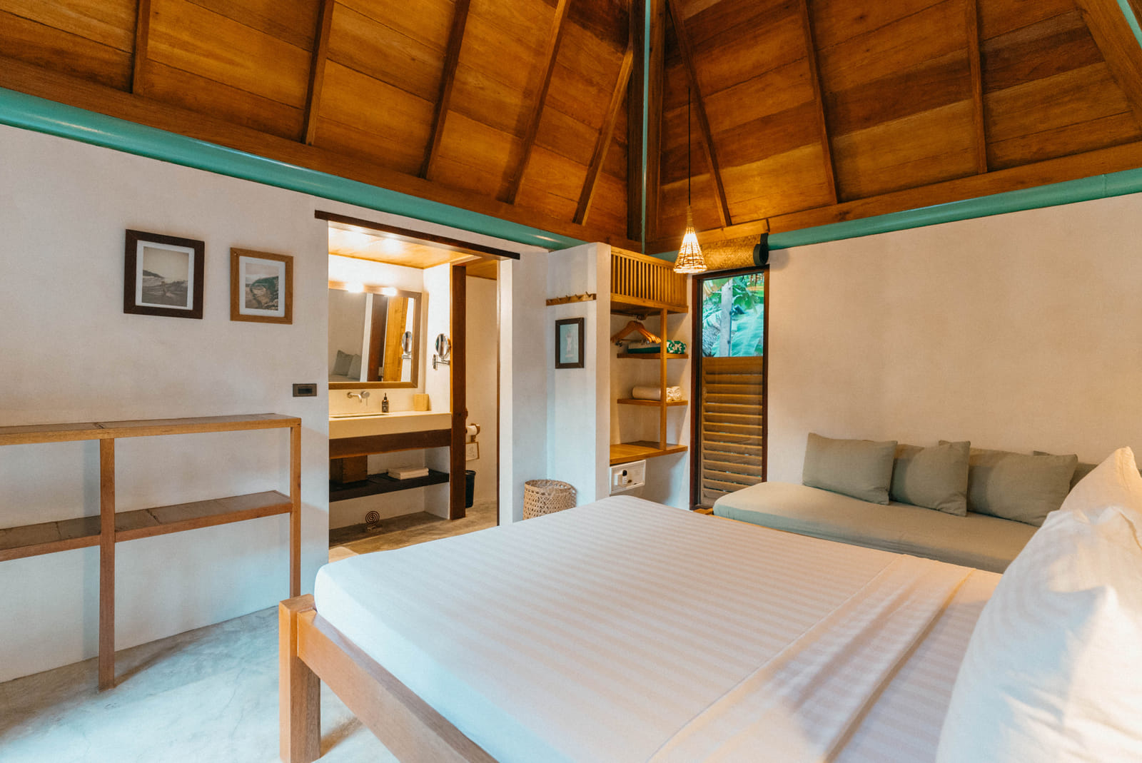 The Double Room bedroom at Bravo Beach Resort Siargao, with a white bed, sage green daybed, and vaulted wood-beamed ceiling, en-suite bathroom beyond