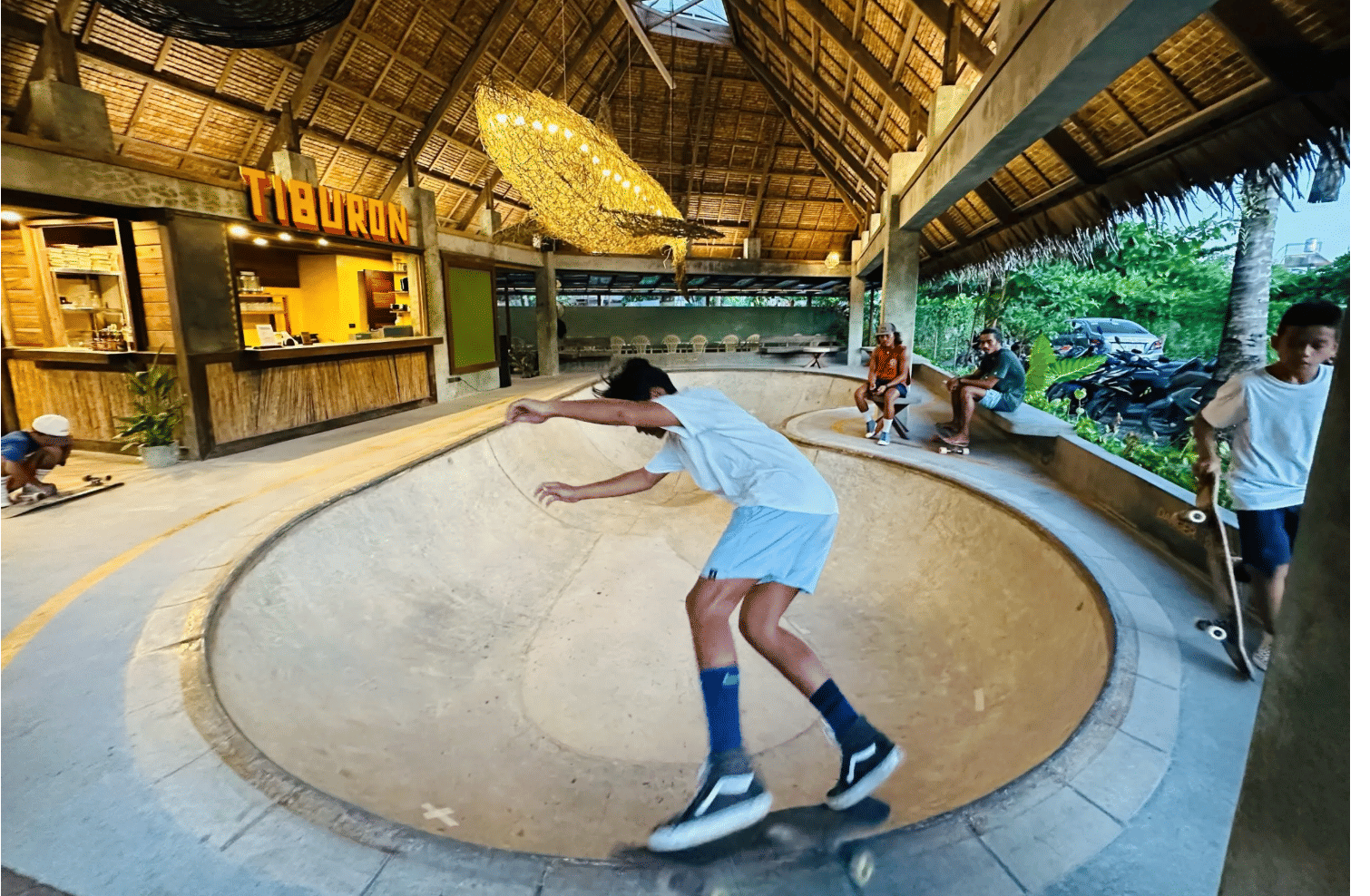 A skater leans into a turn inside the Bravo Beach Resort Siargao skate bowl, beneath a woven chandelier and the Tiburon snack bar sign