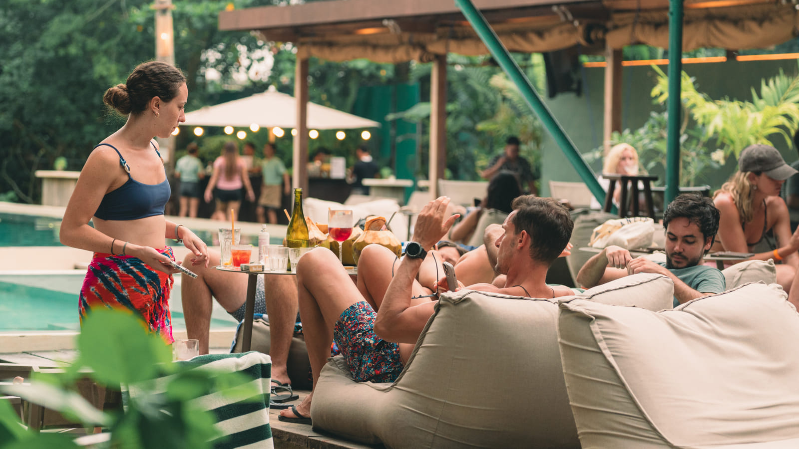 Guests relaxing on beanbags beside the pool at Bravo Beach Resort Siargao, with drinks and snacks on a low table and string lights overhead