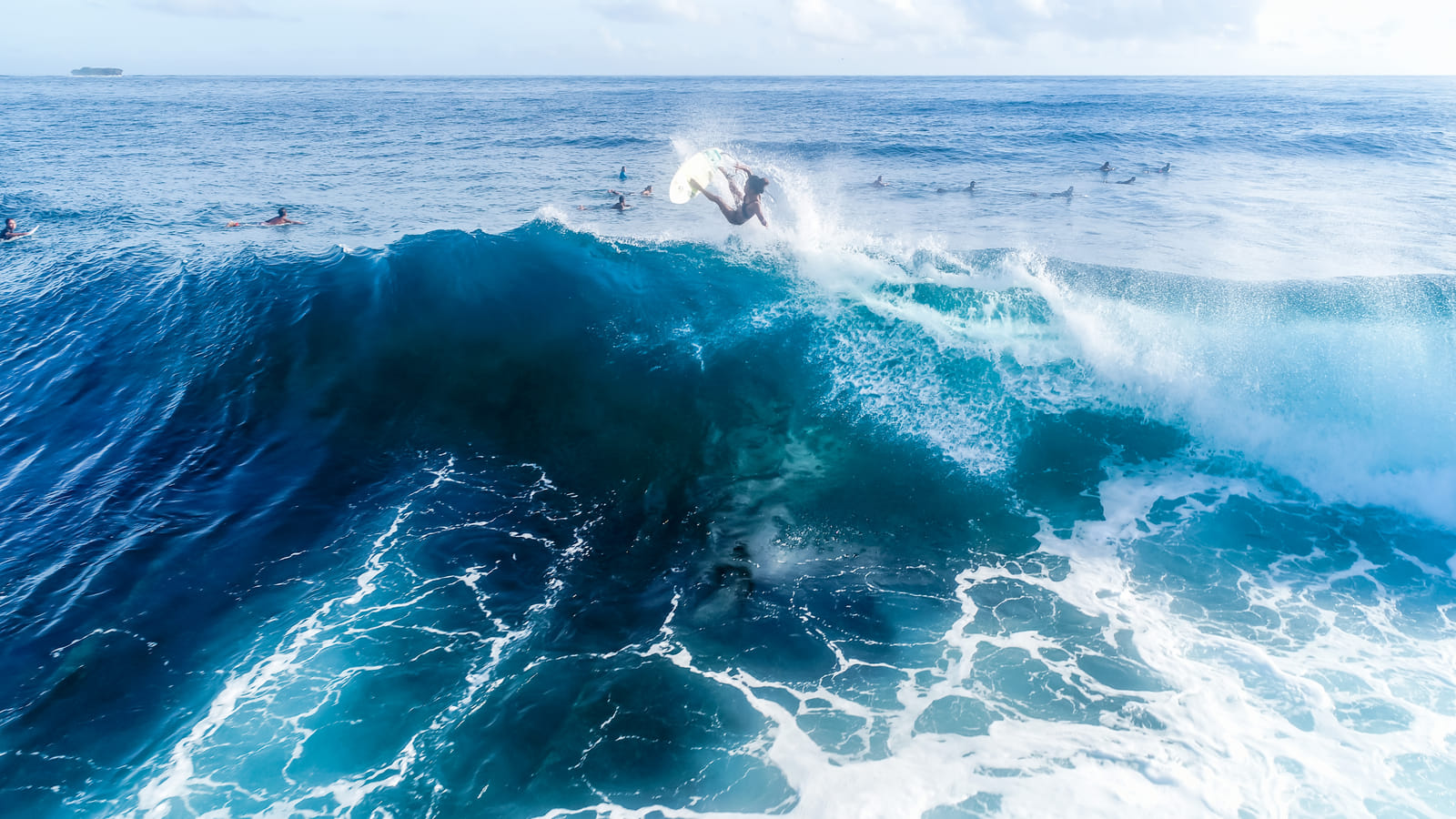 Aerial view of a surfer wiping out off the top of a large breaking wave at Cloud 9, Siargao, while other surfers wait in the lineup nearby