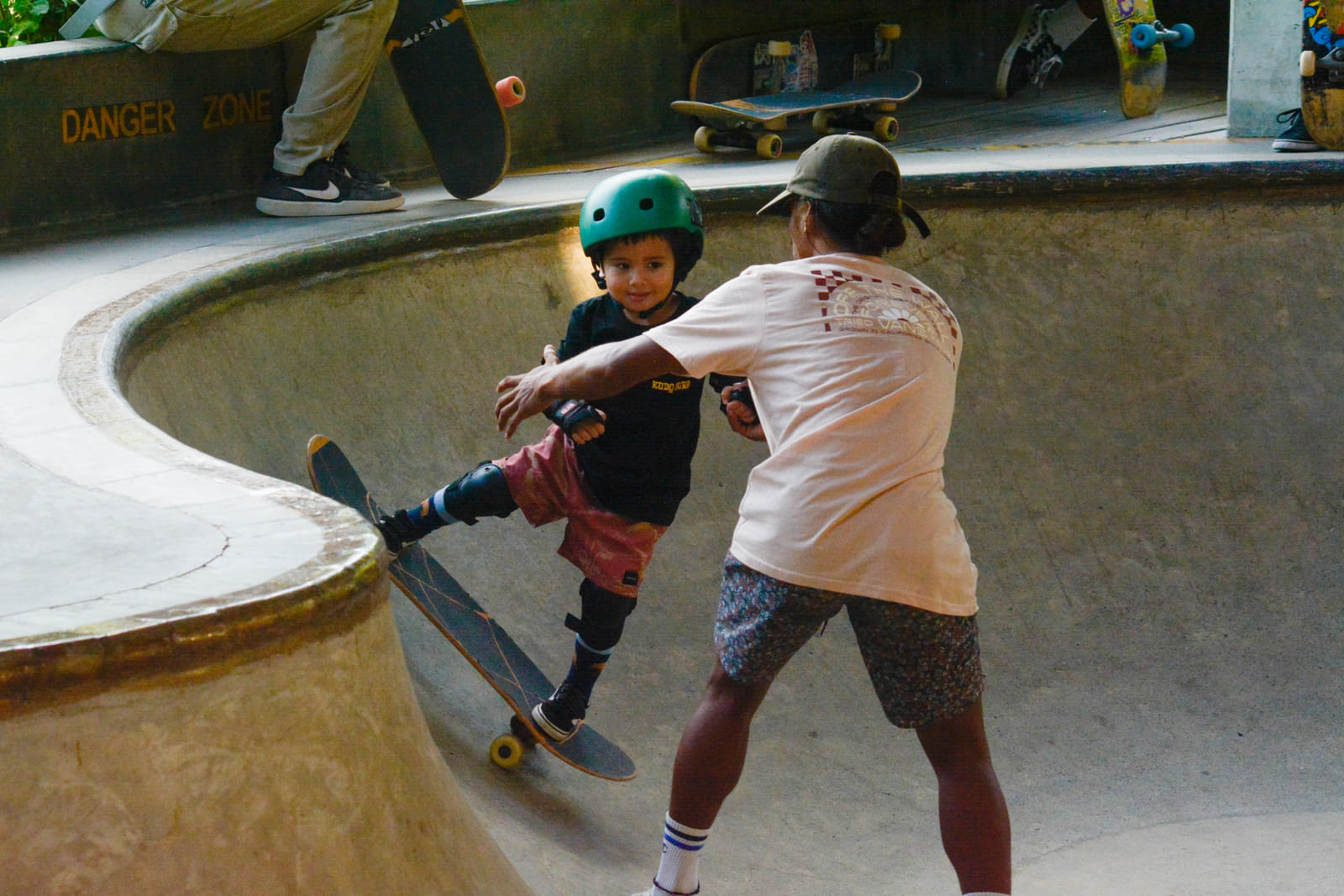 A young skater in a helmet and pads gets a push start into the Bravo Beach Resort Siargao skate bowl from an adult, beside a Danger Zone sign
