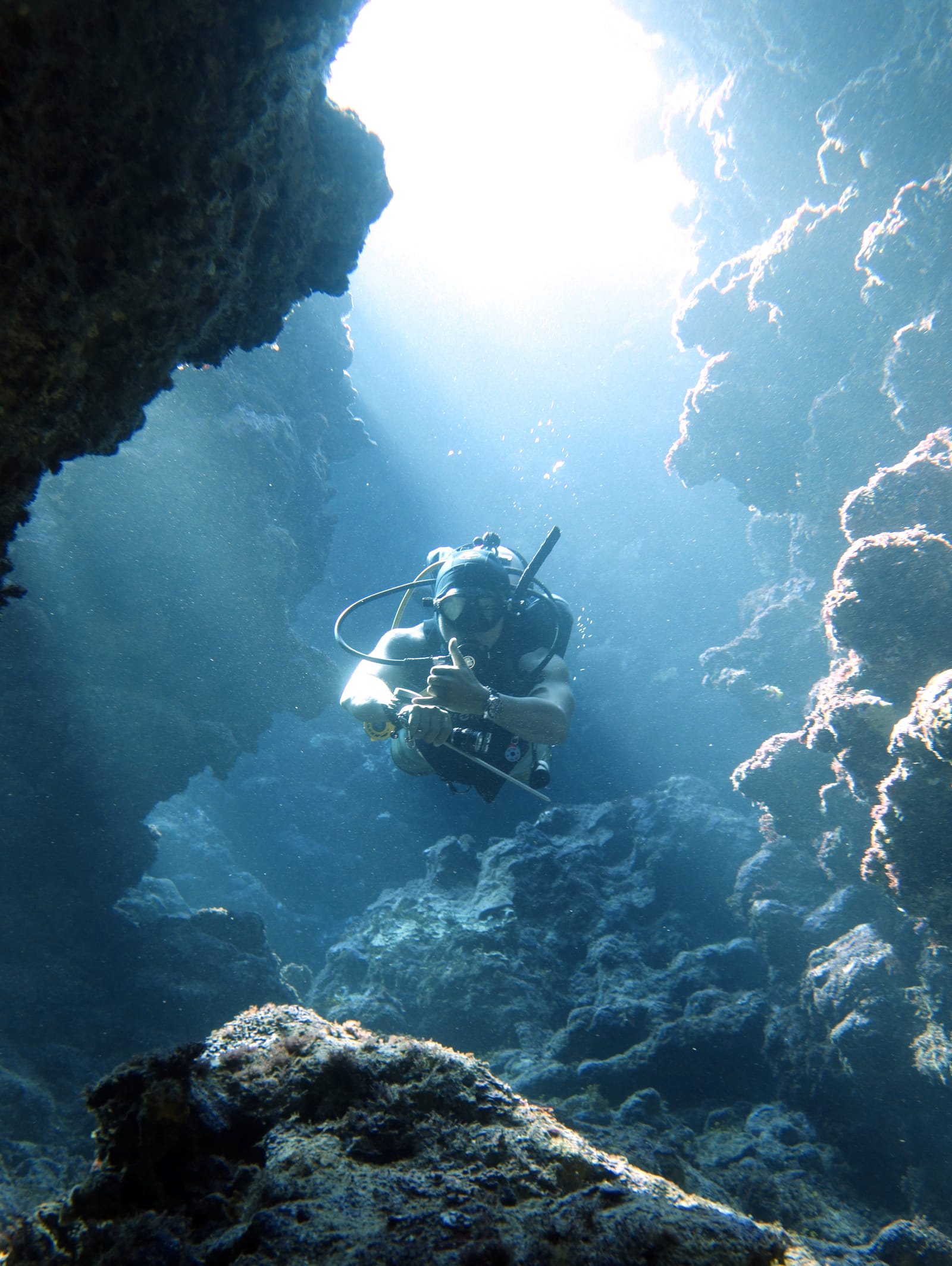 A scuba diver swims through the underwater rock arch at Daku, a dive spot near Siargao, with light streaming down from above