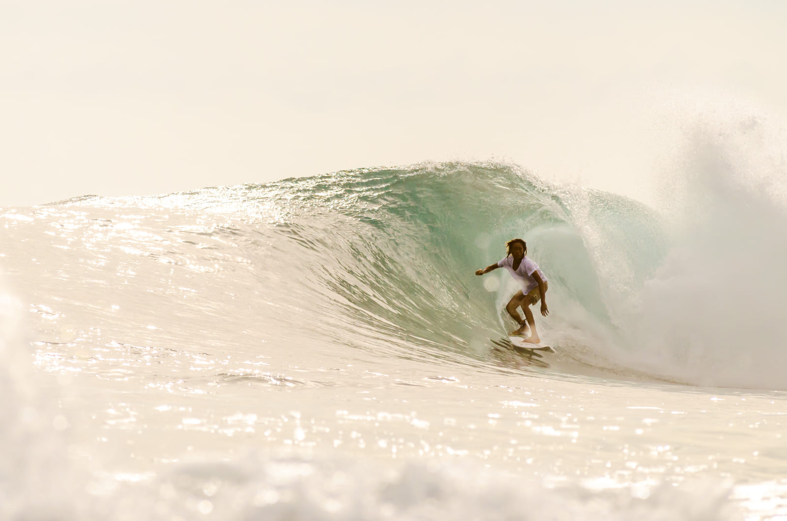 A surfer crouched low inside the curl of a large barreling wave, spray glowing in soft golden backlight at General Luna, Siargao