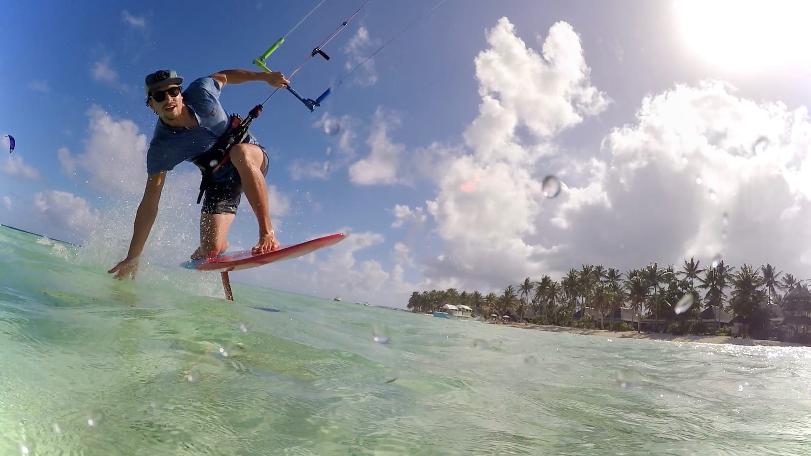 A kitesurfer riding a hydrofoil board across turquoise water, kite lines overhead, with a palm-lined shore in the distance at General Luna, Siargao