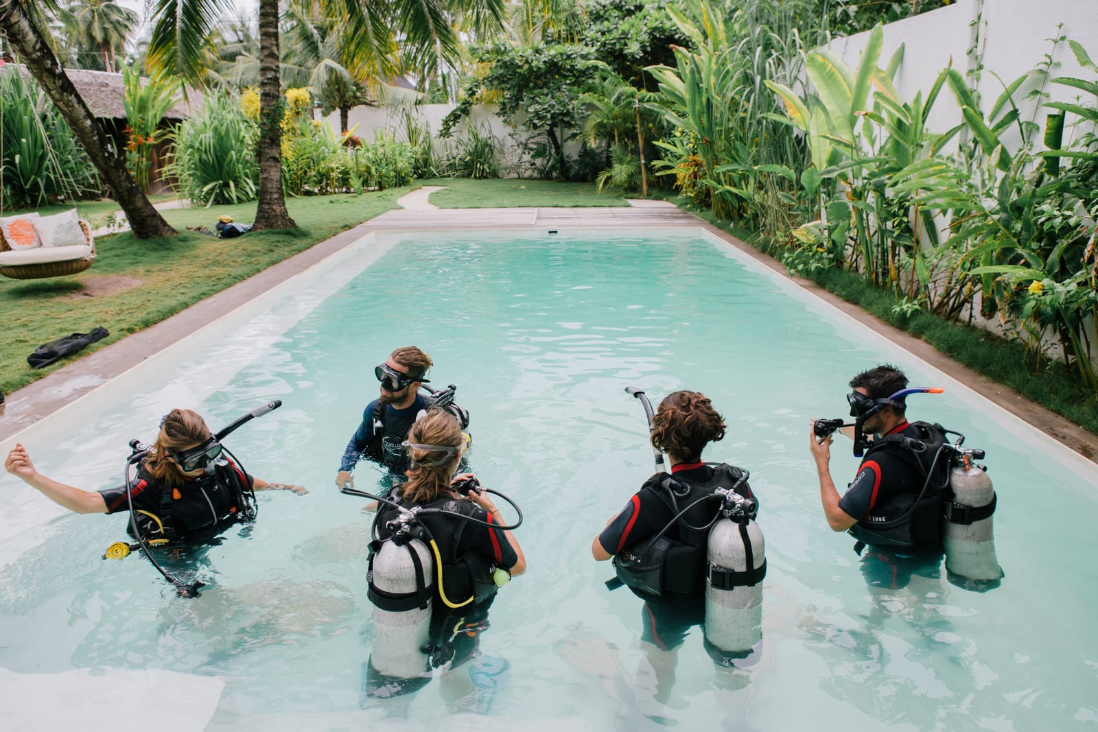 A group of scuba divers with tanks and gear practicing skills in a swimming pool surrounded by a lush tropical garden in Siargao