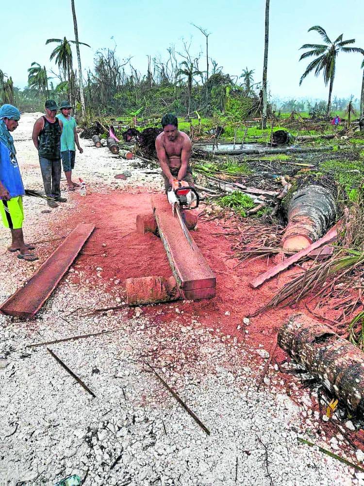A man uses a chainsaw to cut a fallen coconut log into lumber while others watch, amid storm-damaged palm trees in Siargao after a typhoon