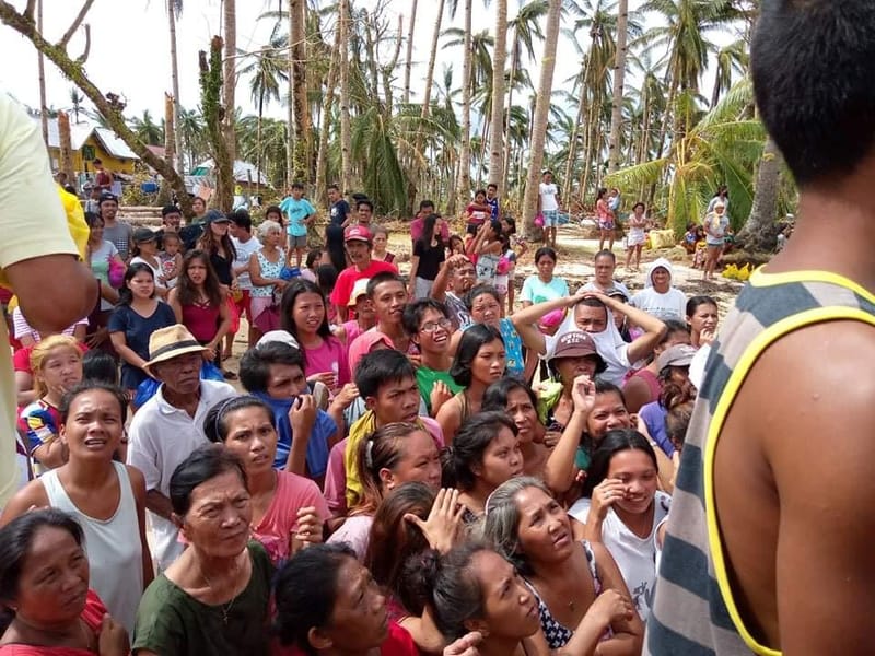 A large crowd of residents gathers outdoors among storm-stripped coconut trees during a community relief operation in Siargao after the typhoon