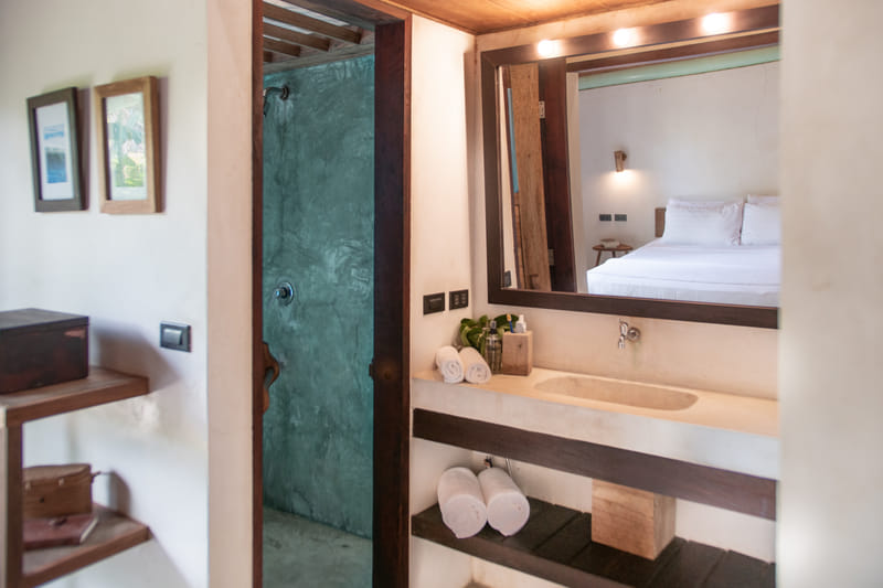 En-suite bathroom at Bravo Beach Resort Siargao with a stone sink, wall mirror reflecting the bed, folded towels, and a teal-tiled open shower