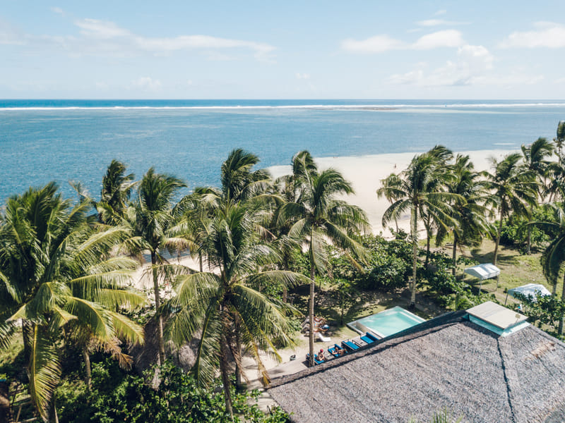 Aerial view of Bravo Beach Resort Siargao showing a thatched-roof building, swimming pool, and coconut palms beside a white sand beach and turquoise sea