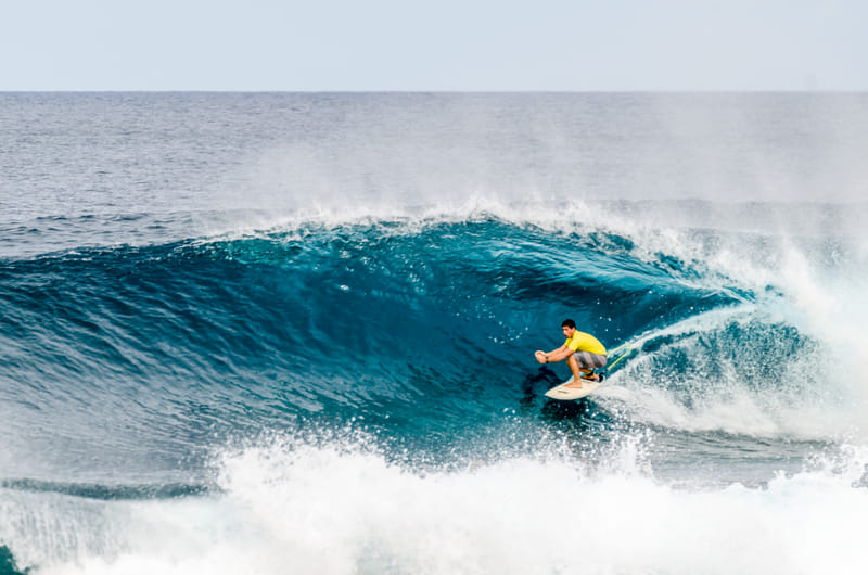 Surfer crouched inside a barreling wave at General Luna, Siargao, spray whipping off the crest above him