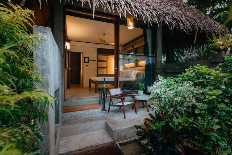 Garden Room exterior at Bravo Beach Resort Siargao with thatched roof and private patio holding wooden chairs and a table amid greenery