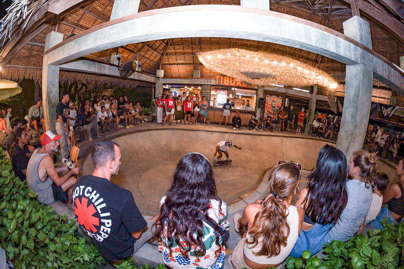 Crowd watching a skater in the Bravo Skate Bowl Jam at night, under a thatched roof lit with string lights
