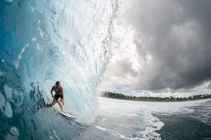 Female surfer riding inside a barreling wave with the coastline visible under a cloudy sky at Cloud 9, Siargao
