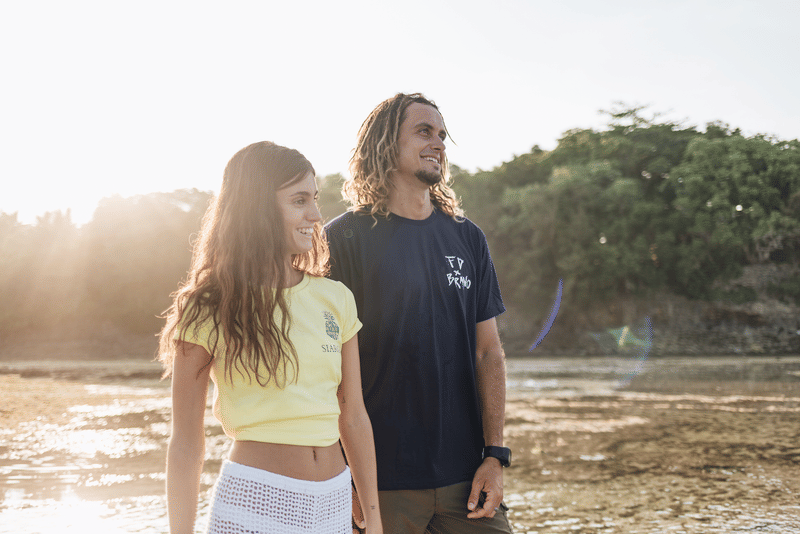 A young man and woman walking and smiling together along a shallow tidal flat at golden hour, with mangrove trees in the background in Siargao