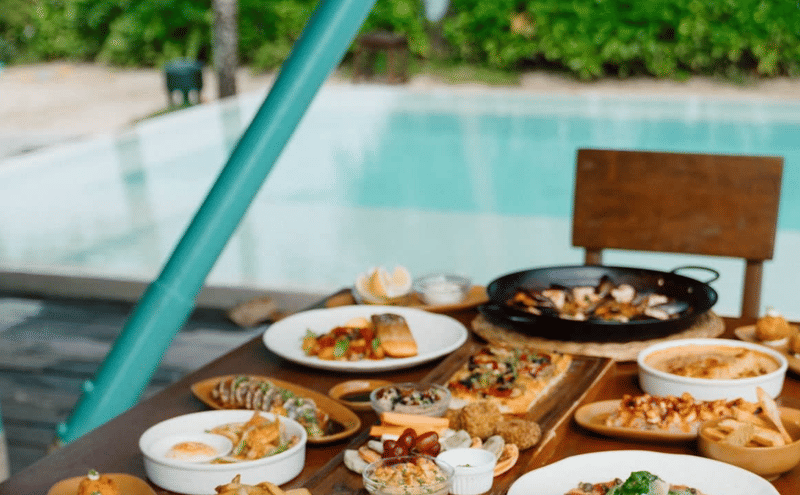 Bravo Beach Resort Siargao poolside table spread with grilled fish, flatbread, seafood paella, and assorted mixed appetizers