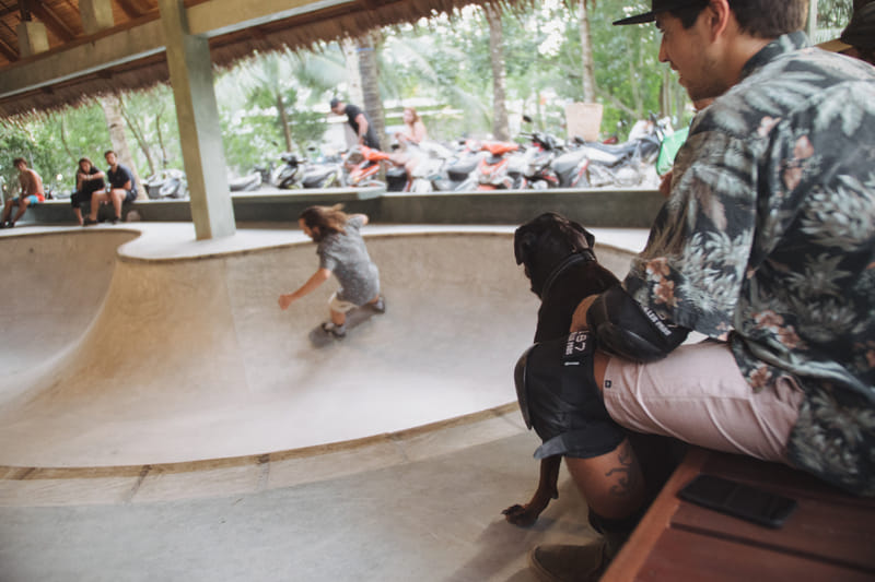 A skater riding the concrete skate bowl at Bravo Beach Resort Siargao, watched by spectators and a dog under a thatched-roof shelter