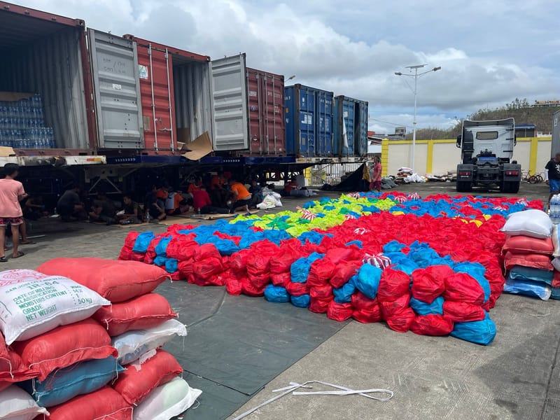 Rows of colorful relief supply bags arranged near shipping containers and trucks as part of a large-scale relief operation in Siargao