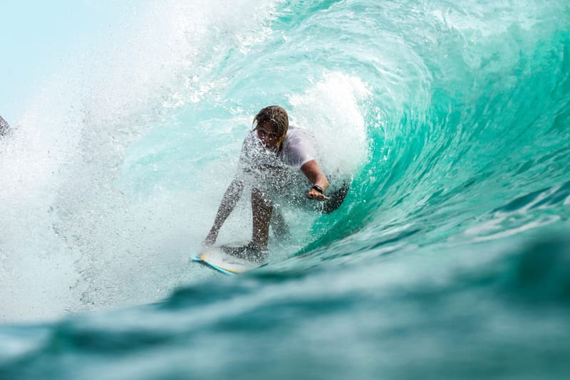 A surfer crouches low on his board while riding deep inside the hollow barrel of a curling turquoise wave off General Luna, Siargao
