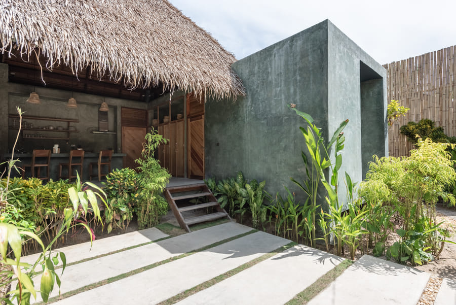 The entrance to Tadhana Villa at Bravo Beach Resort Siargao, with a thatched roof, concrete steps, and lush tropical landscaping around a tiled path