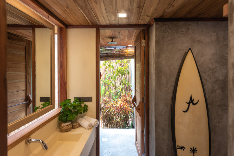 The vanity at Tadhana Villa, Bravo Beach Resort Siargao, with a mirror, potted plant, and a view to an open-air shower with surfboard decor