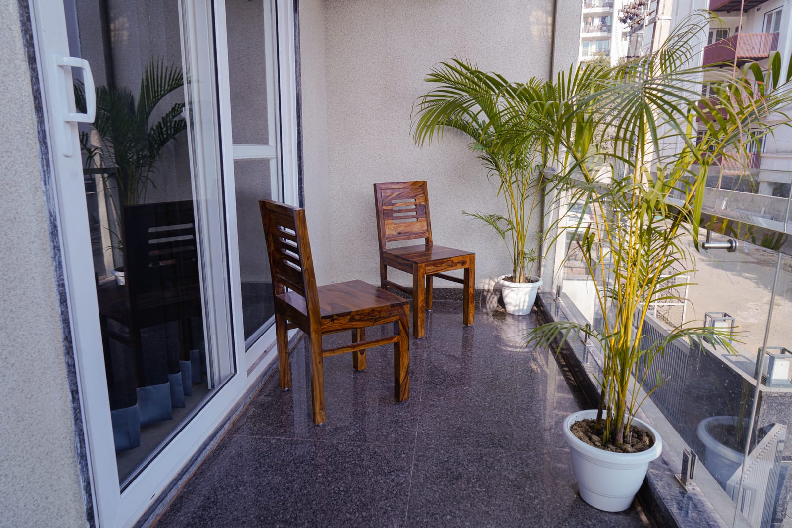 Balcony with two wooden chairs and potted palms at Lime Tree 2BHK Serviced Apartment, Golf Course Road