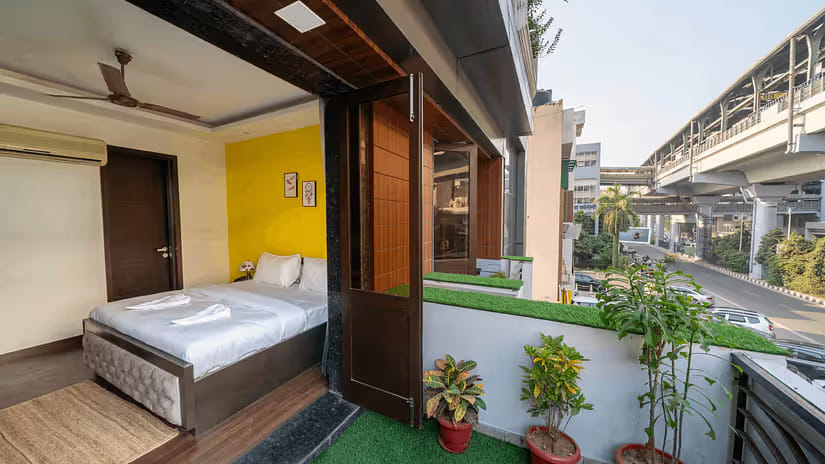 Bedroom opening to a balcony with plants and a view of the metro line at Lime Boutique Bed and Breakfast, Kailash Colony
