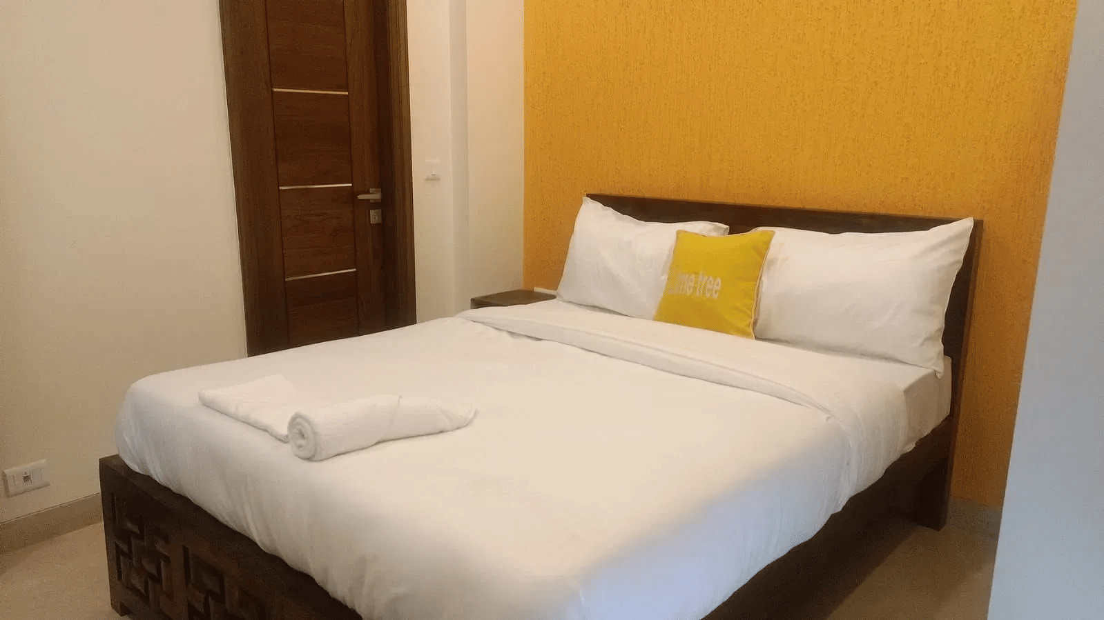 Bedroom with a double bed and yellow accent wall at Lime Tree 1BHK Serviced Apartment Near Medanta