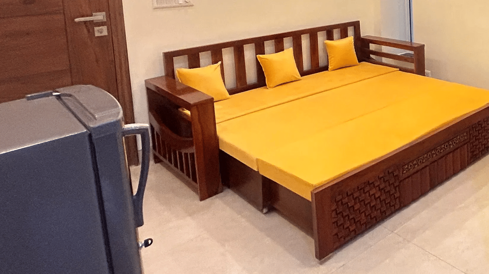 Deluxe Room (1BHK) with a wooden sofa cum bed and yellow cushions at Lime Tree Serviced Apartment, Sector 39, Gurgaon
