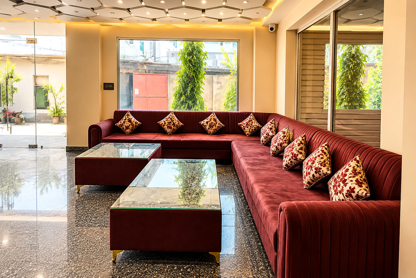 Lobby lounge with a maroon L-shaped sofa and garden view at Lime Tree Hotel & Banquet, Jaipur