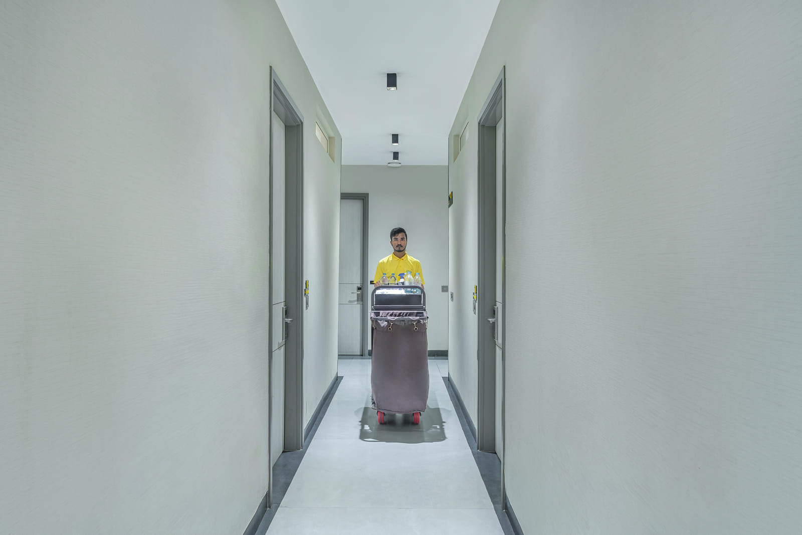 Hotel corridor with room doors and a staff member pushing a luggage trolley at Y Stay by Lime Tree Hotels, Greater Noida