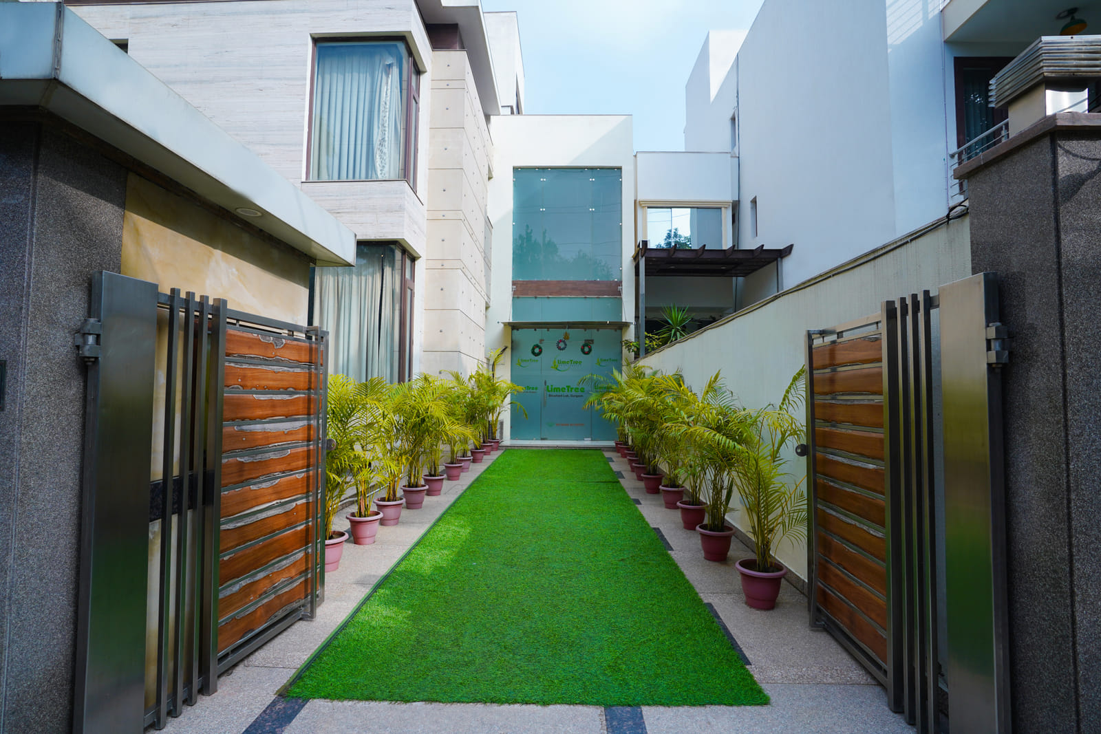 Entrance walkway with artificial grass, potted plants and wooden gates at Lime Tree Hotel, IFFCO Chowk