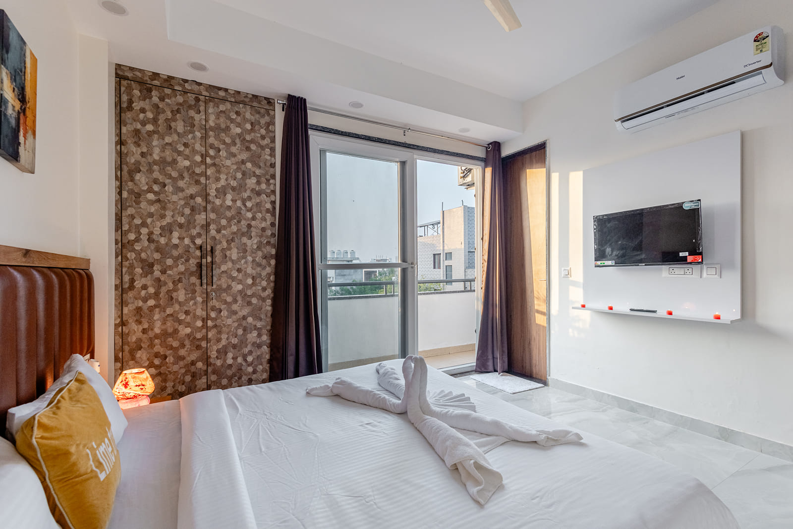 Bedroom with a white bed, wall-mounted TV, wardrobe and balcony door at Lime Tree Luxury 2BHK Serviced Apartment