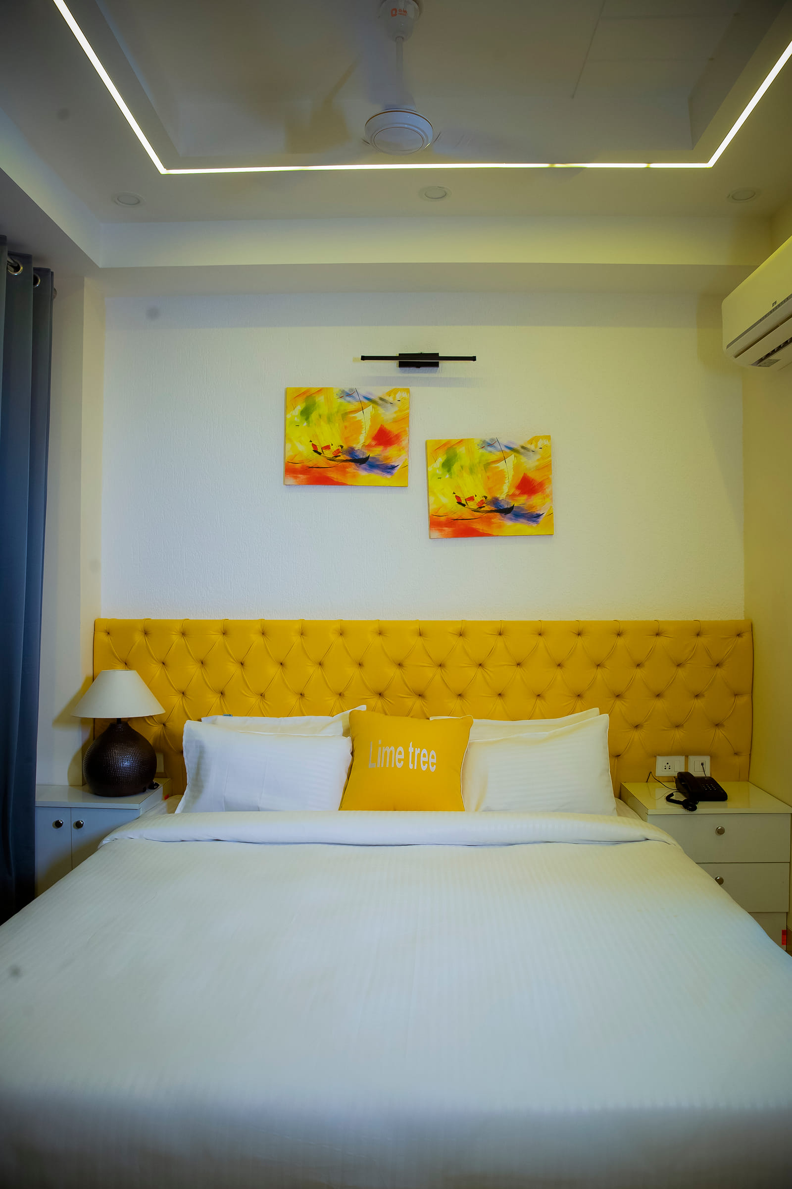 Bed with a tufted yellow headboard, abstract paintings and bedside lamp at Lime Tree Luxury Studio