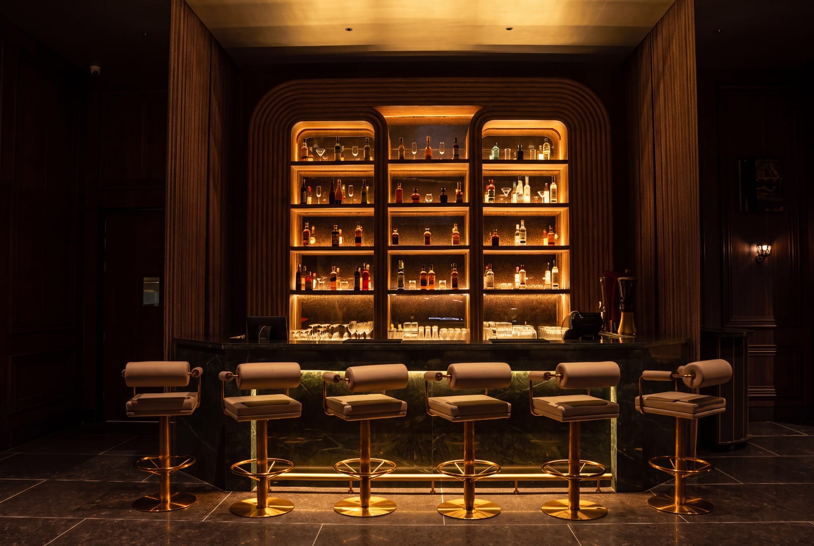 Bar counter with backlit shelves of bottles, cushioned bar stools and a stone-tiled floor at Azul Lounge & Bar, RG Grand Hotel & Convention.