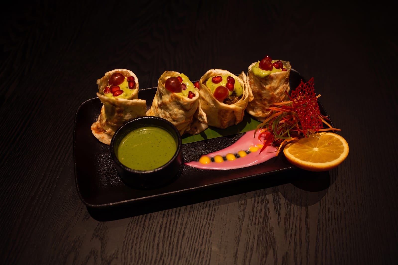 Stuffed rolls on a dark plate with green dip, pink sauce and orange slices on a wooden table at Azul Lounge & Bar, RG Grand Hotel & Convention.