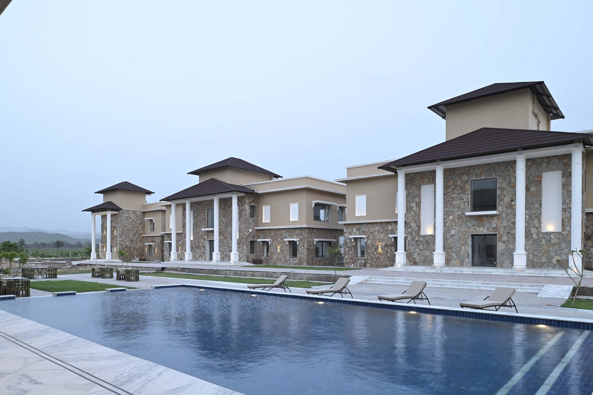 Pool with loungers in front of the stone facade, hills in the distance at dusk