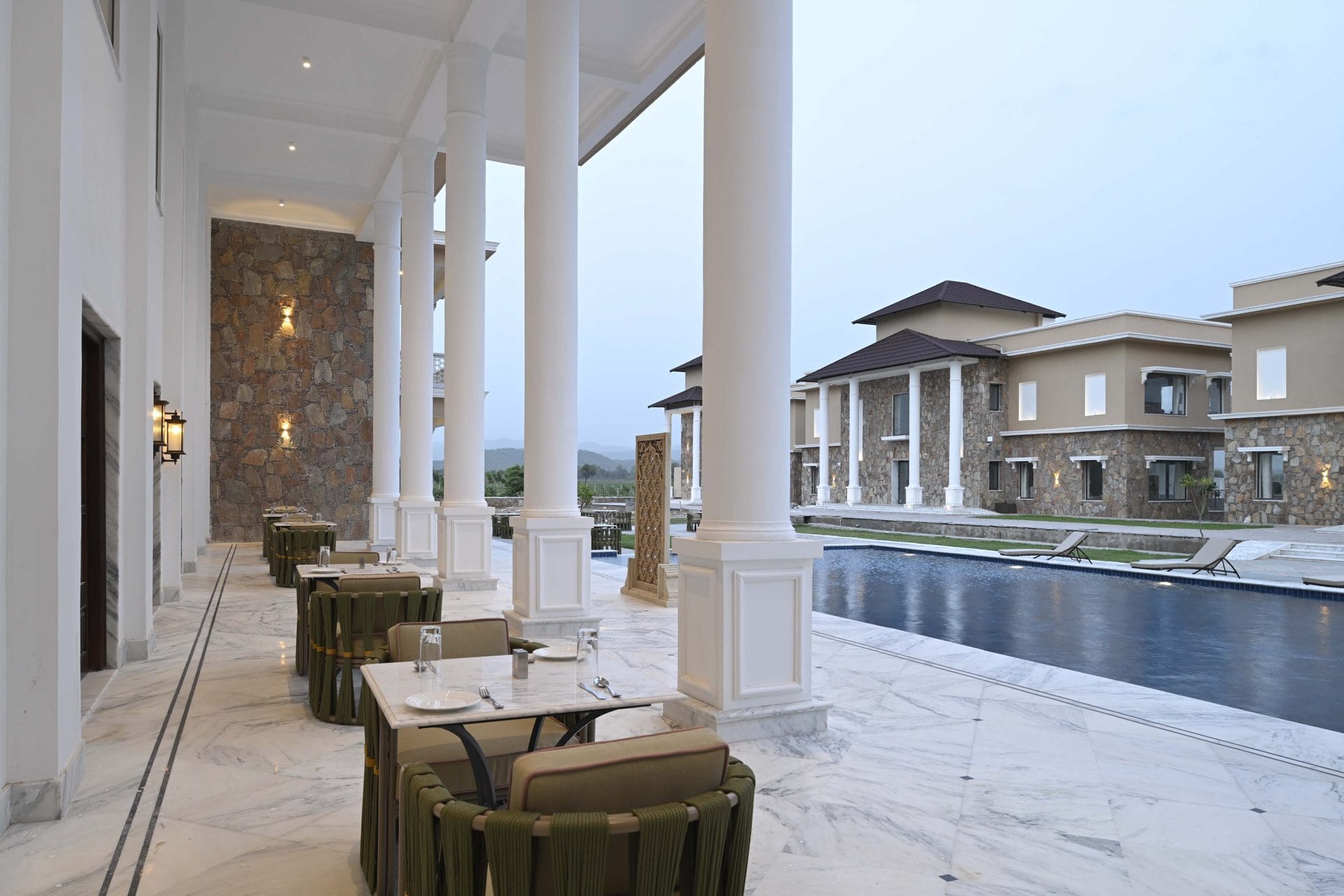 Dining tables on the marble colonnade beside the pool, villas behind at dusk