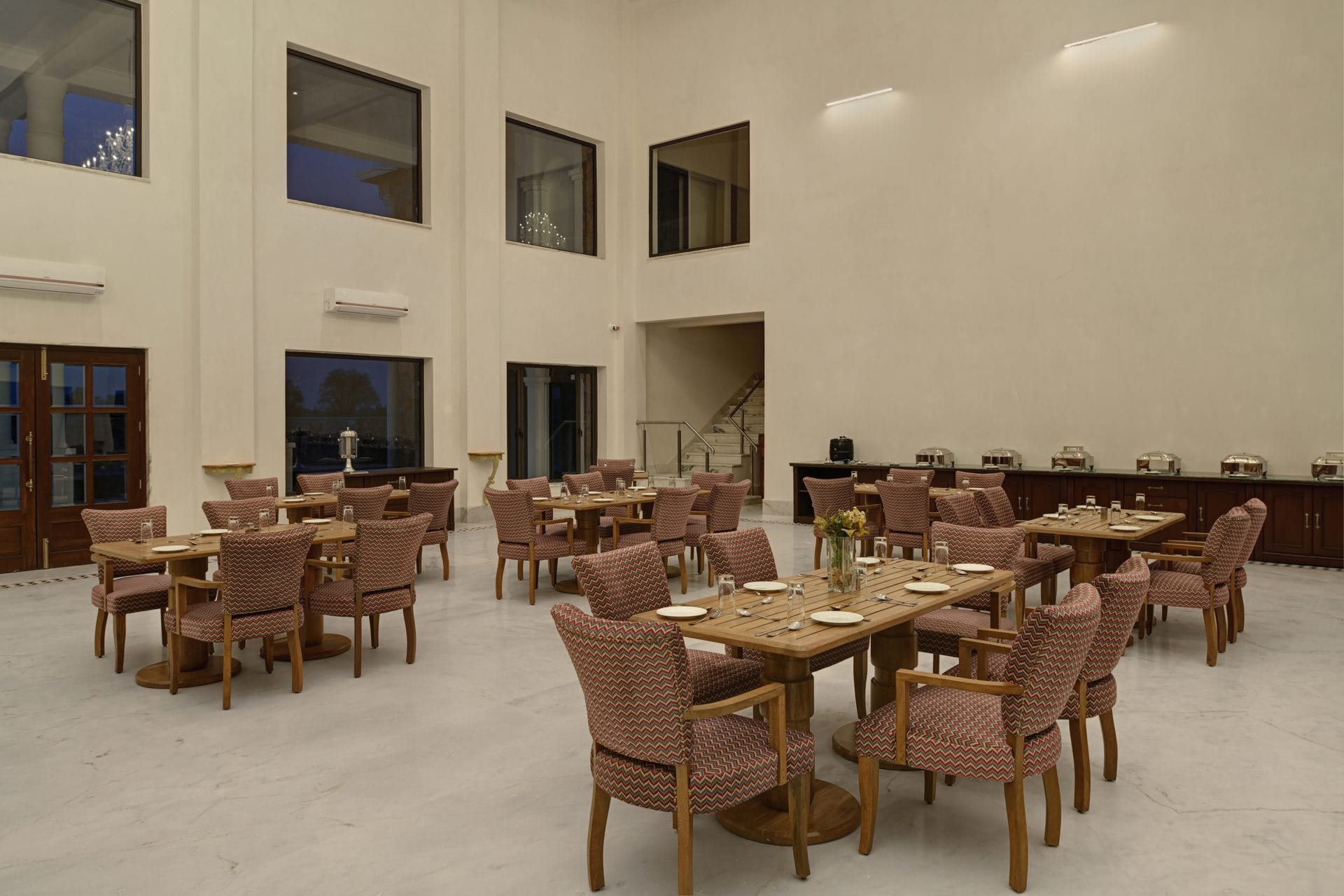Dining hall at dusk with tall windows and set tables
