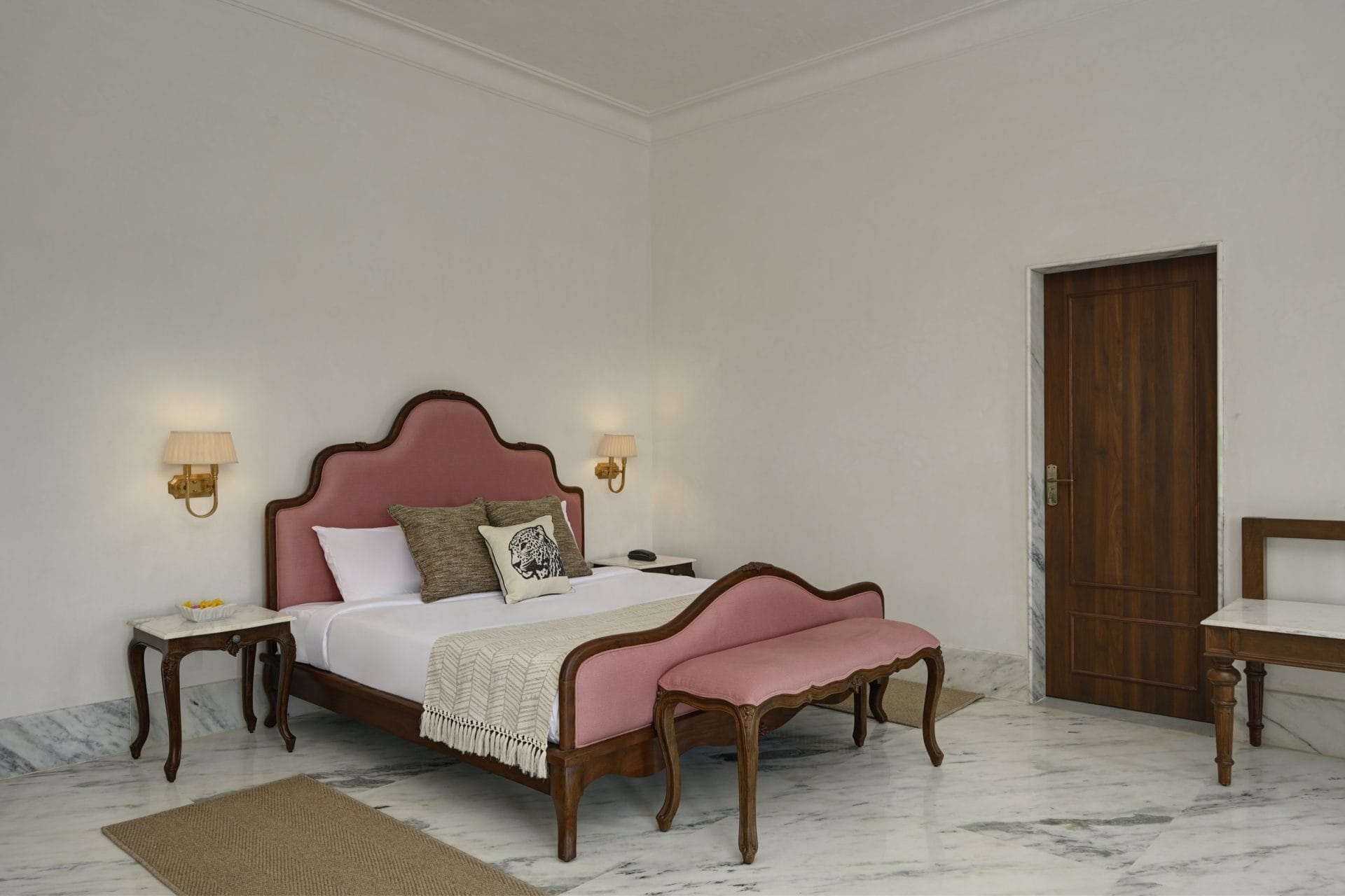 Suite bedroom with a pink upholstered bed, wall lamps, and a wooden door