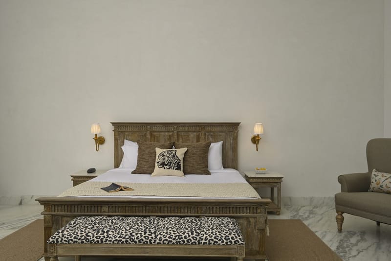 Carved wooden headboard, leopard-print cushion, and bench at the foot of a Deluxe bed
