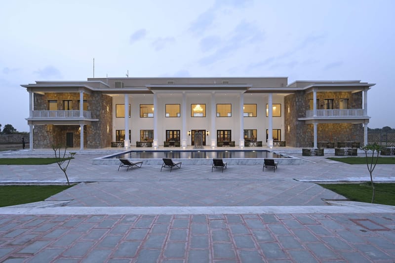 Front facade at dusk with lit windows, the pool, and 4 loungers on the forecourt